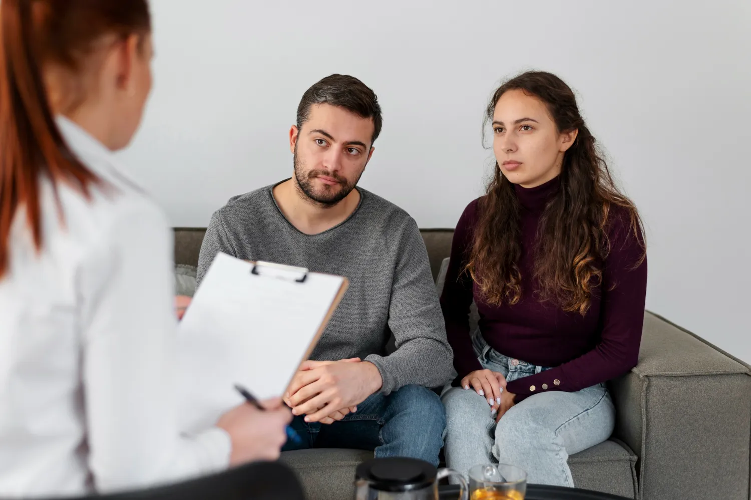 Pareja en una sesión de terapia con un profesional, mostrando atención y preocupación, en un ambiente cómodo y acogedor.