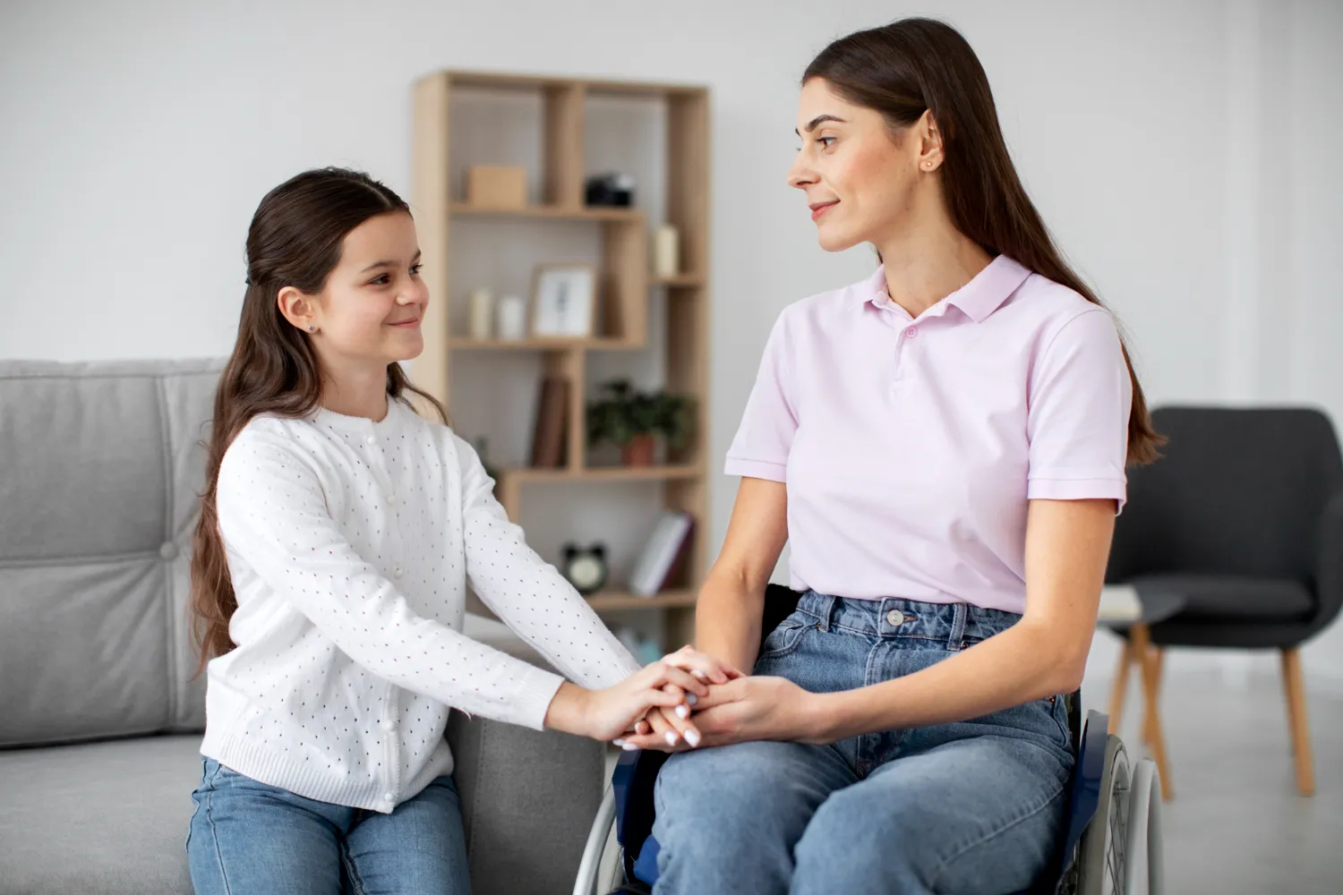 Mujer en silla de ruedas interactuando con una niña en un ambiente acogedor, mostrando una conexión emocional y apoyo mutuo. Ideal para temas de inclusión y relaciones familiares.